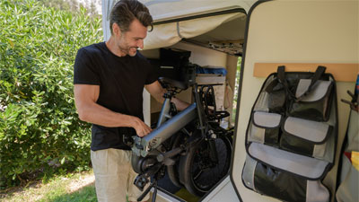 Un homme range son vélo pliable dans un camping-car.