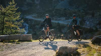 Un couple roule en VTT sur une piste cyclable, avec un paysage montagneux en arrière-plan.
