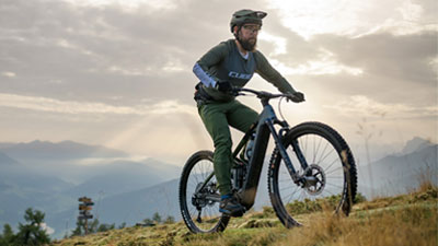 On voit un homme sur un VTT électrique Cube Stereo Hybrid gris qui roule sur un sentier de randonnée.
