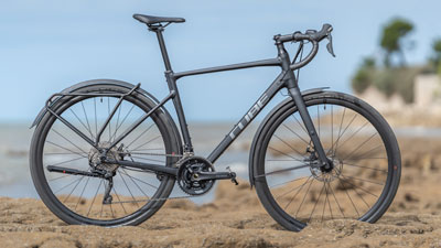On voit un vélo de Cube de Gravel noir, posé sur un sol rocailleux, avec la côte en arrière-plan.